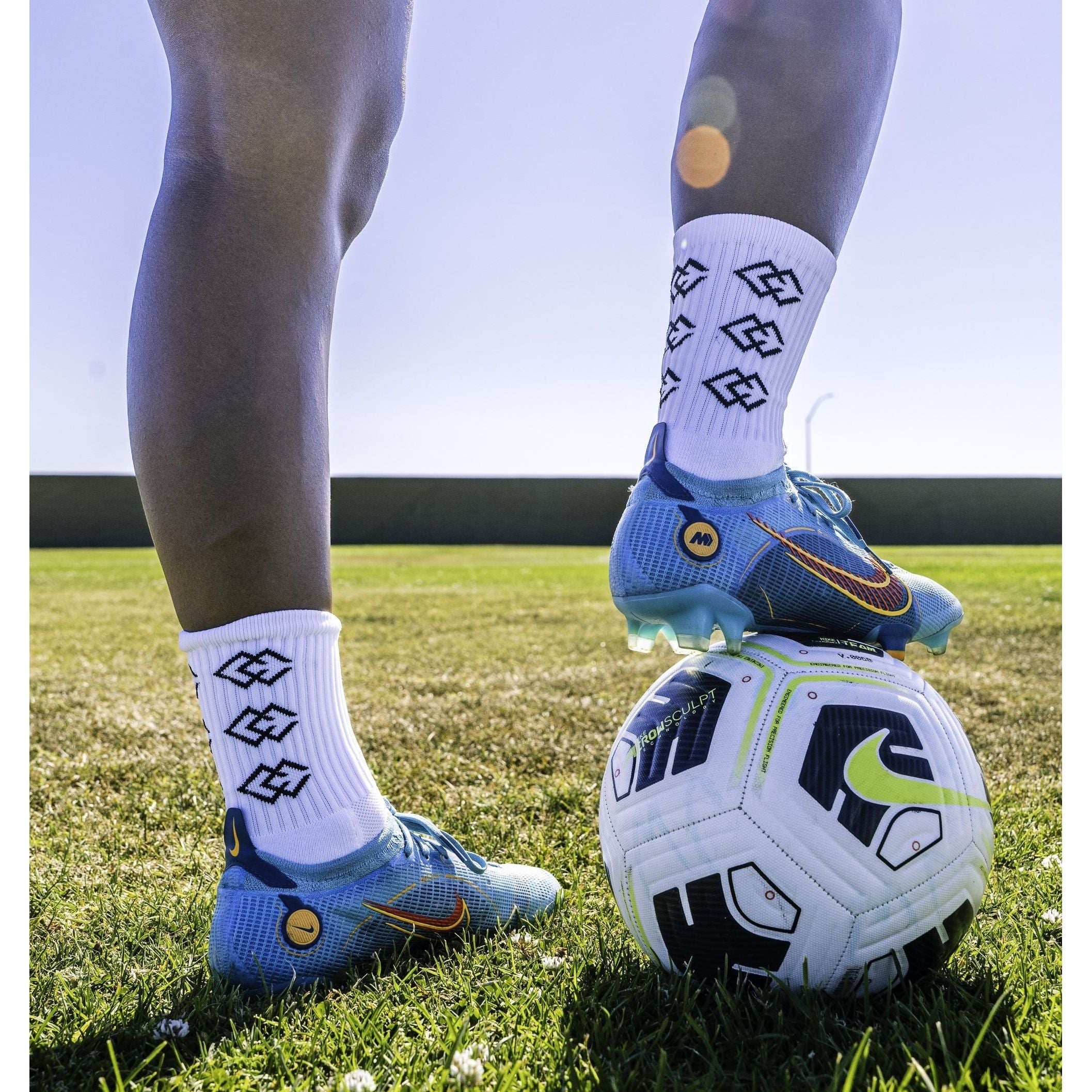 Player wearing white C3 grip socks and blue soccer cleats with one foot on a soccer ball