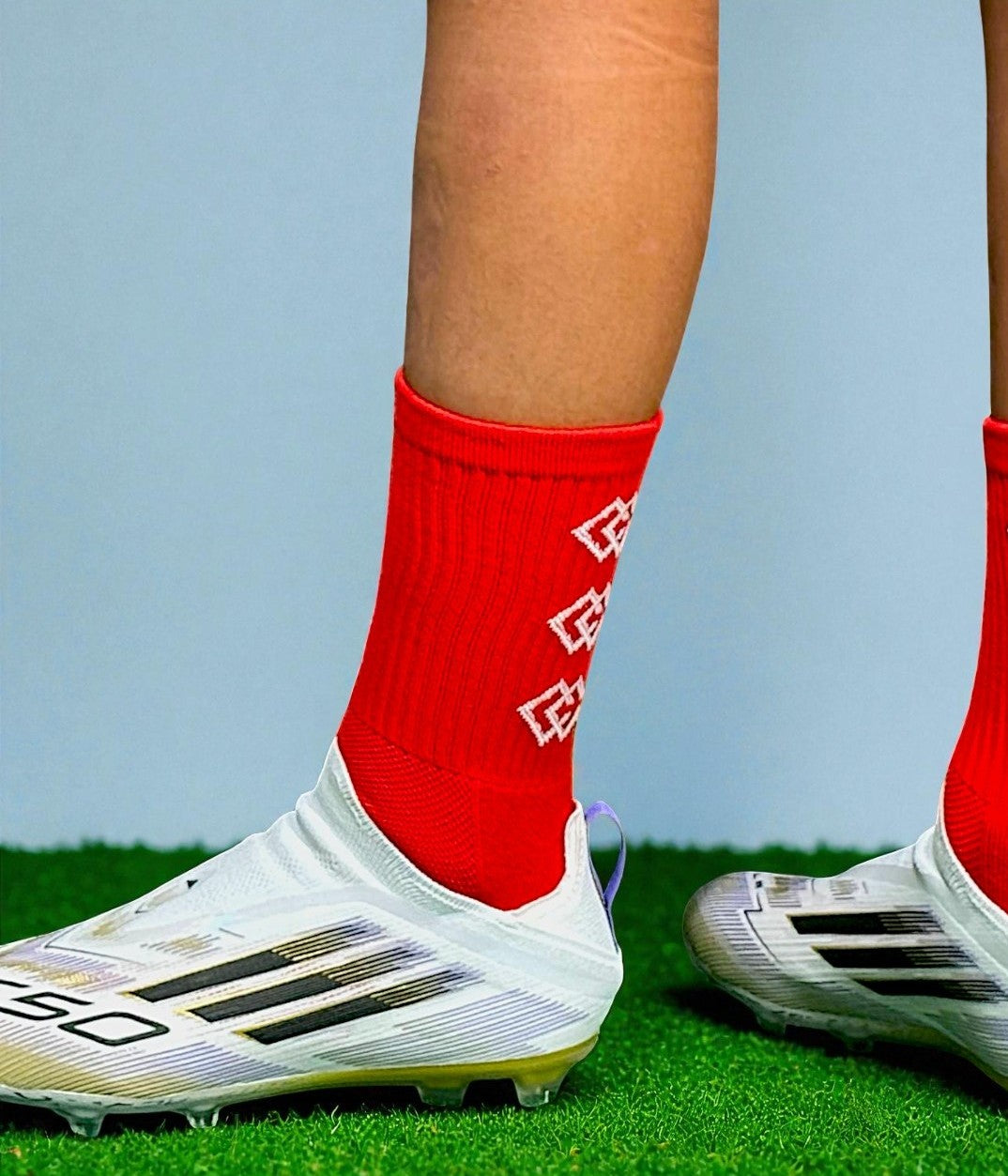 Player wearing red C3 grip socks with white soccer cleats on green turf