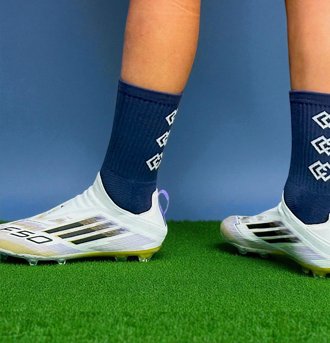 Player wearing navy C3 grip socks with white soccer cleats on green turf