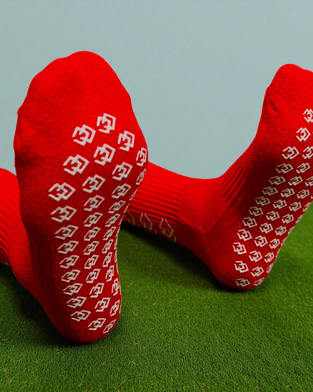 Soles of red C3 grip socks showing the white C3 logo grip pattern on turf