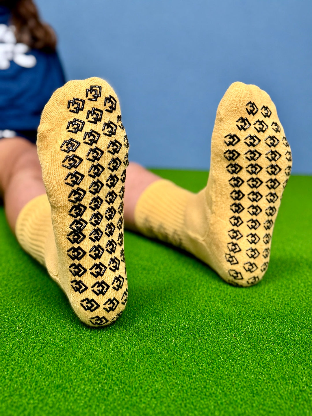 Soles of gold C3 grip socks showing the black C3 logo grip pattern on turf