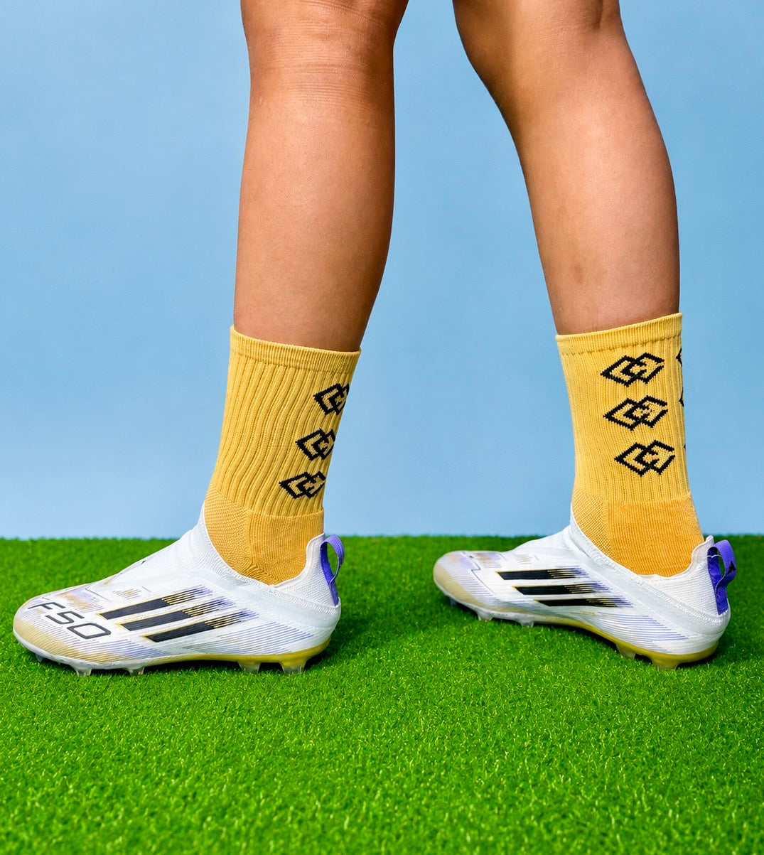 Player wearing gold C3 grip socks with white soccer cleats on green turf