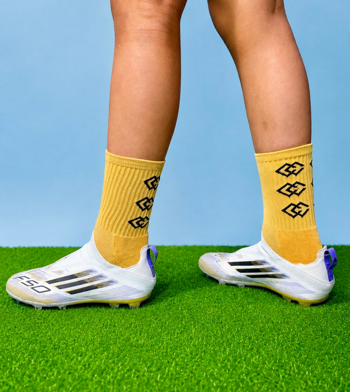 Player wearing gold C3 grip socks with white soccer cleats on green turf