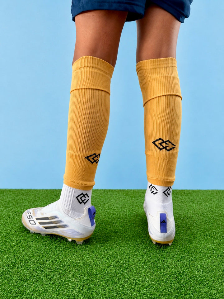 Rear view of a player wearing gold C3 pre-cut socks over white C3 grip socks on turf