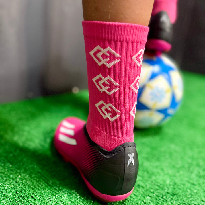 Close-up of a player wearing pink C3 grip socks with black and pink soccer cleats on turf