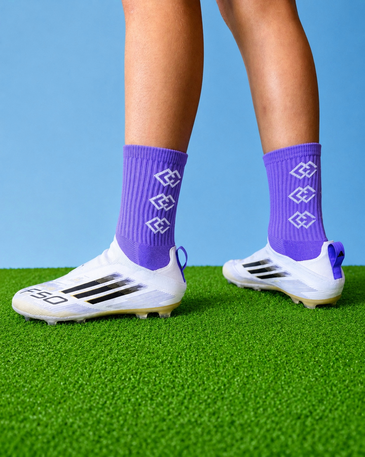 Player wearing purple C3 grip socks with white soccer cleats on green turf